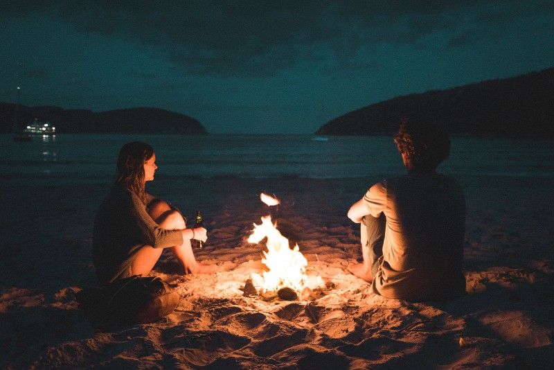 Mann und Frau sitzen am Meer in der Nähe des Lagerfeuers