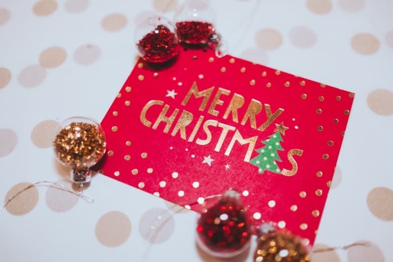 Weihnachtskarte in der Nähe von roten und goldenen Ornamenten