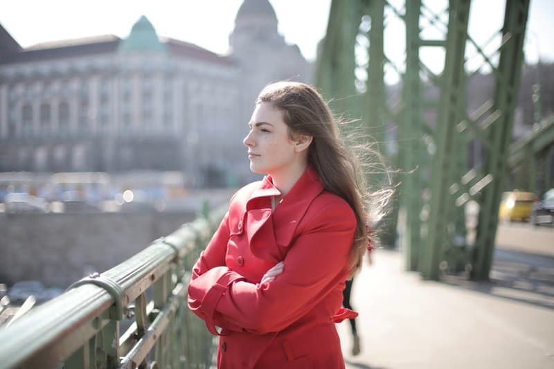 Frau auf der Brücke denkt nach und trägt einen roten Mantel