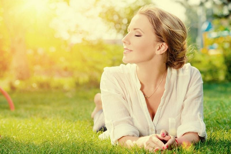 Schöne lächelnde Frau, die auf einem Gras im Freien liegt. Sie ist absolut glücklich.