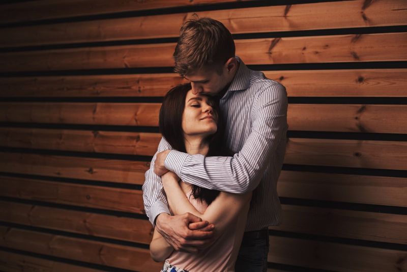 Mann umarmt Frau, während er in der Nähe einer Holzwand steht