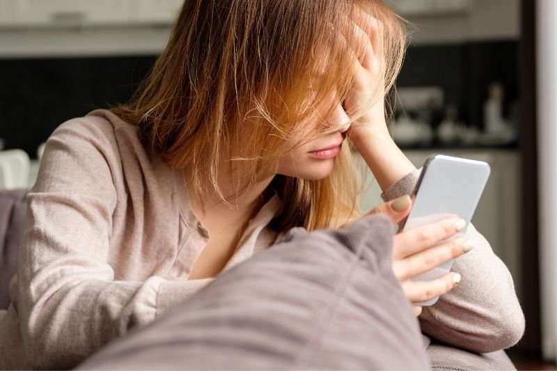 Verärgerte Frau lehnt auf der Couch und schaut auf ihr Smartphone im Wohnzimmer
