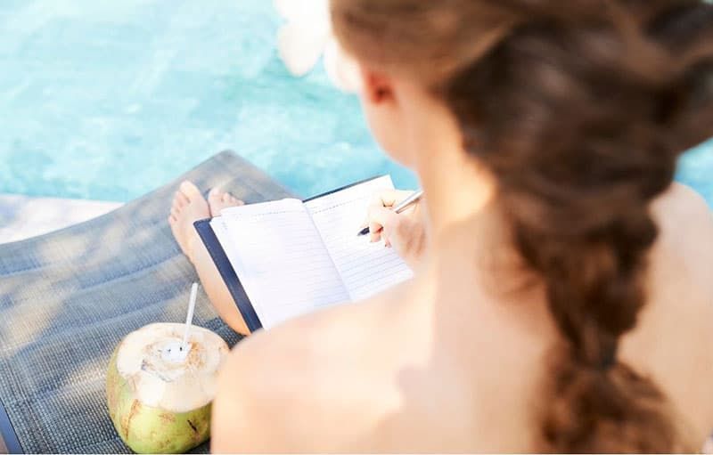 Draufsicht auf eine Frau, die in der Nähe eines Schwimmbads Tagebuch schreibt