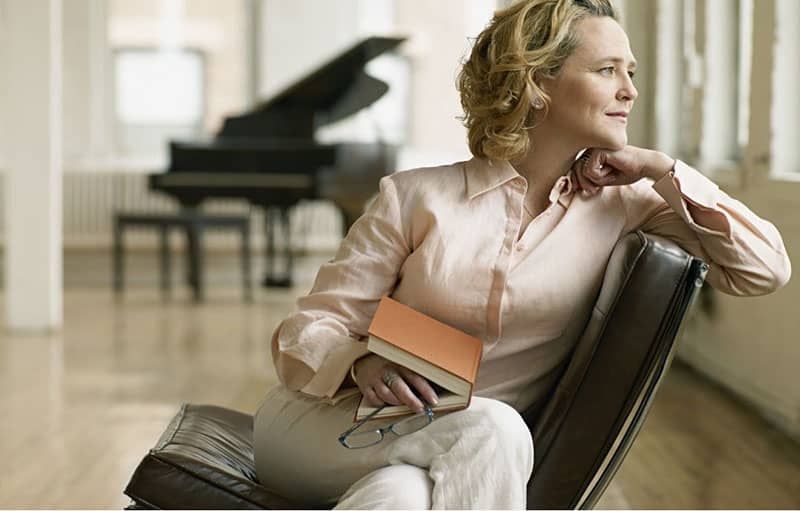 Erwachsene Frau denkt, sie sitzt mit einem Buch auf dem Schoß und einem Klavier in einiger Entfernung