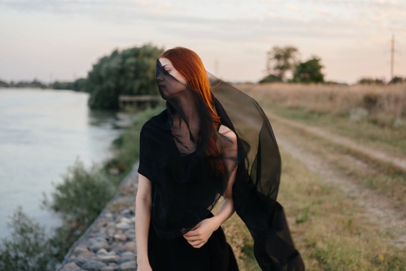 Frau in einem dunklen Kleid und mit einem schwarzen Schleier in der Nähe des Flusses