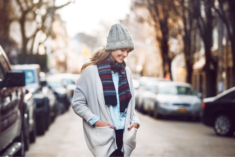 Eine lächelnde Frau in einem Pullover mit Mütze und Schal geht die Straße entlang