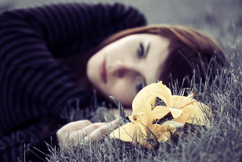 ein trauriges Mädchen, das im Gras liegt und eine gelbe Blume in der Hand hält