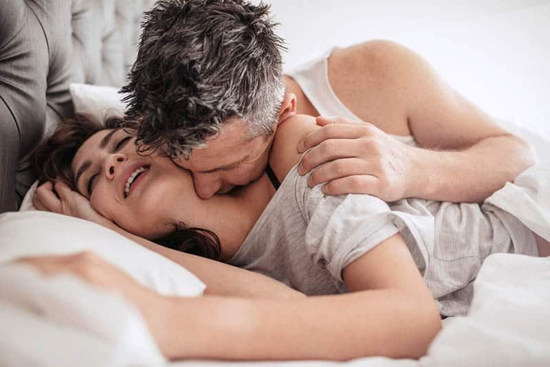 Mann küsst Frau im Schlafzimmer auf den Hals