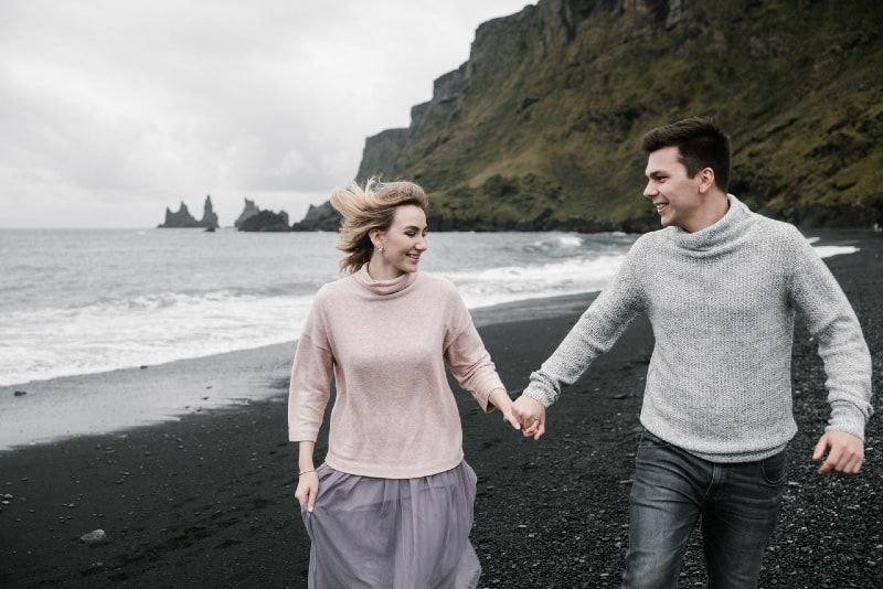 Lächelnder Mann und Frau halten Händchen beim Spaziergang am Meeresufer