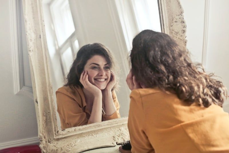 lächelnde Frau im gelben Oberteil, die in den Spiegel schaut