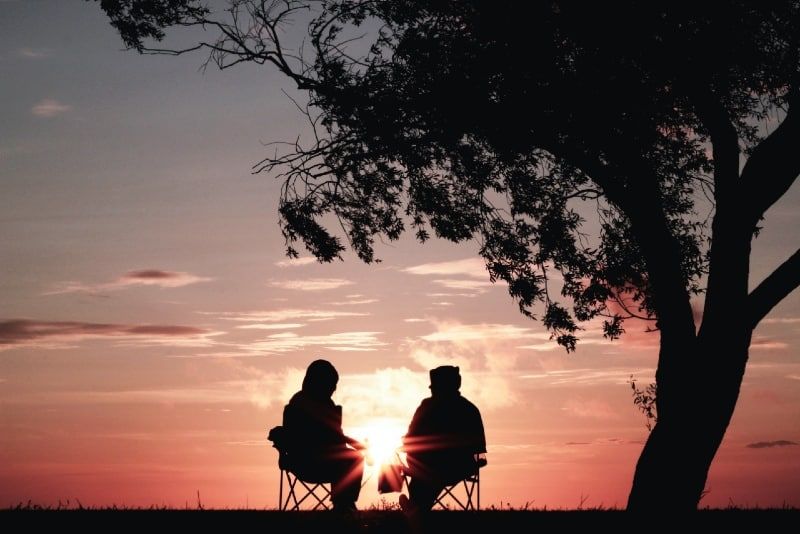 mann und frau sitzen bei sonnenuntergang auf stühlen in der nähe von bäumen