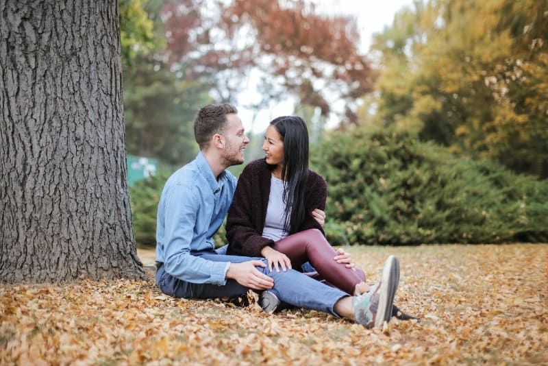 Mann und Frau sitzen auf Blättern unter dem Baum
