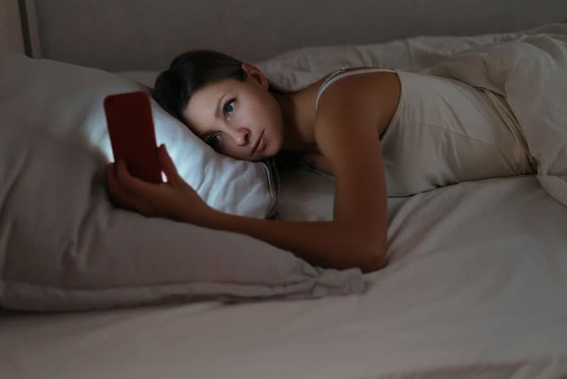 Frau liegt auf einem weißen Kissen und schaut auf ihr Telefon