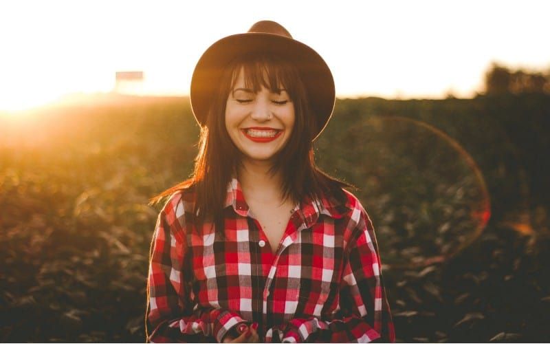 Glückliche Frau mit schwarzem Hut auf einem Feld bei Sonnenuntergang