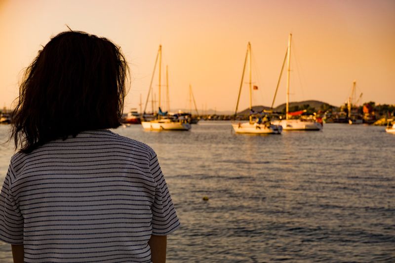 Frau, die bei Sonnenuntergang allein an der Küste des Seehafens sitzt