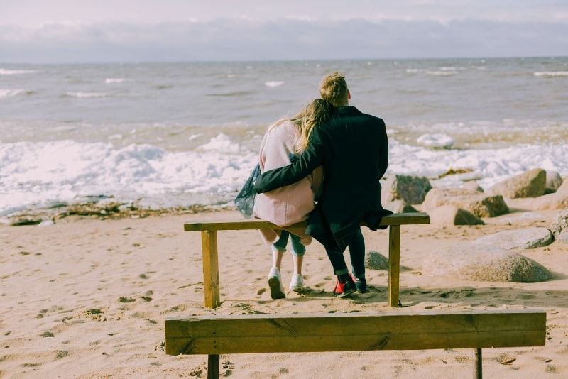 Mann und Frau sitzen auf einer Bank und schauen aufs Meer