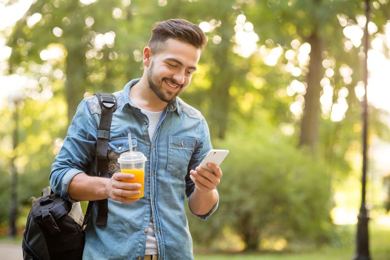 Ein lächelnder junger Mann geht und benutzt ein Smartphone