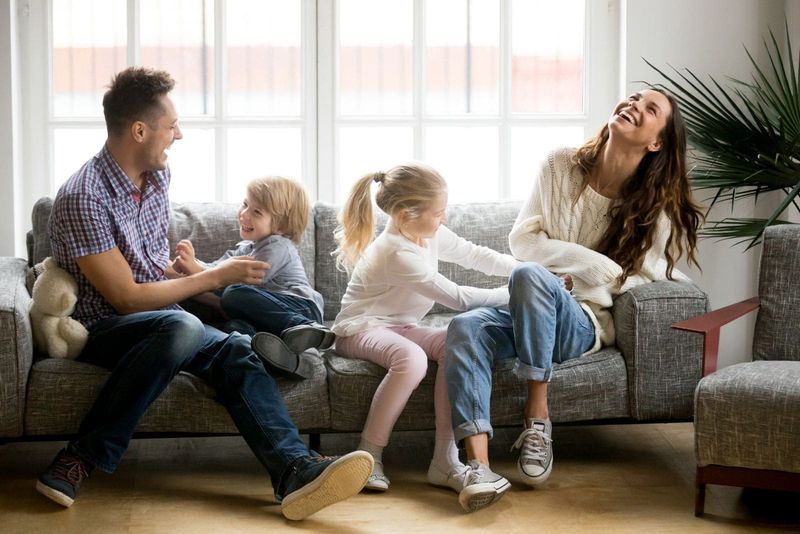 Fröhliche Familie spielt im Wohnzimmer und sitzt lachend auf dem Sofa