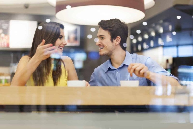 Ein lächelnder Mann und eine lächelnde Frau sitzen da, trinken Kaffee und reden