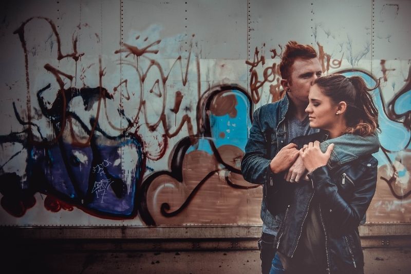 Mann küsst und umarmt Frau, während er in der Nähe einer Graffitiwand steht
