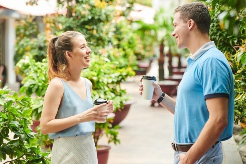 Junger Mann und Frau unterhalten sich auf dem Gehweg und bringen im Stehen eine Tasse Kaffee