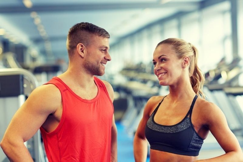 mann und frau im fitnessstudio reden und lächeln und tragen sportbekleidung