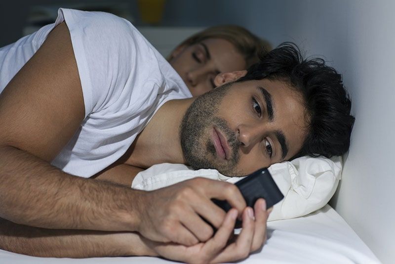 Mann schreibt SMS, während Frau schläft