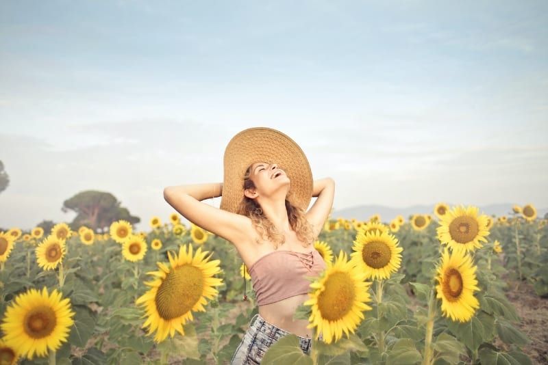 Frau mit Hut steht auf Sonnenblumenfeld