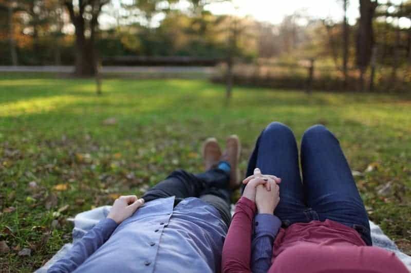 Paar hält Händchen, während es im Gras liegt