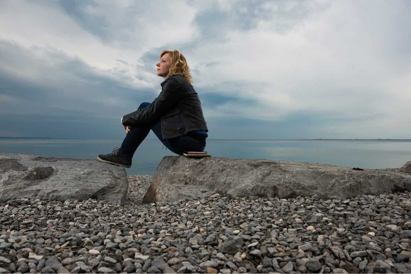 Frau sitzt auf einem Felsen und blickt auf das Meer