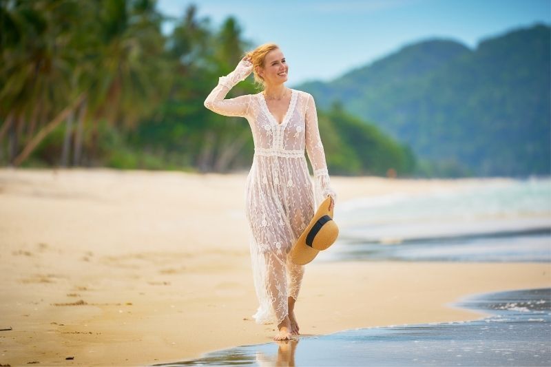 Glückliche Frau im Urlaub, die an einem heißen Sommertag am Strand entlang spaziert