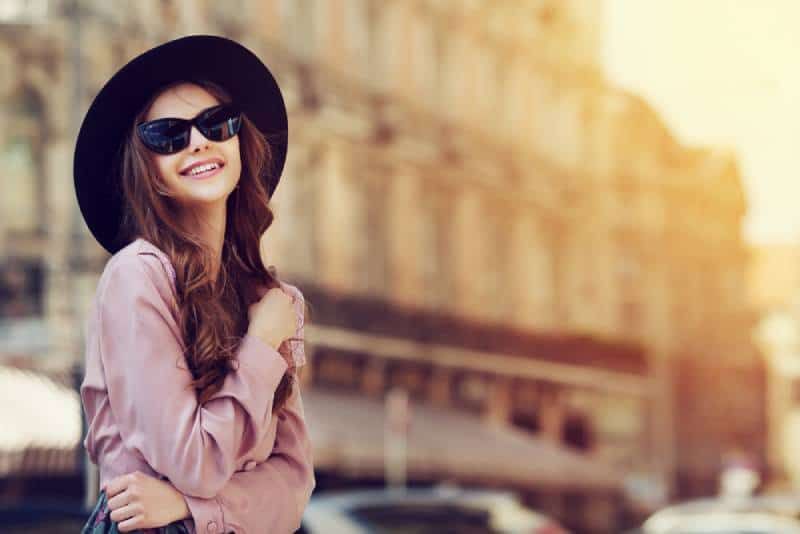 Lächelnde Frau mit schwarzem Hut und Sonnenbrille