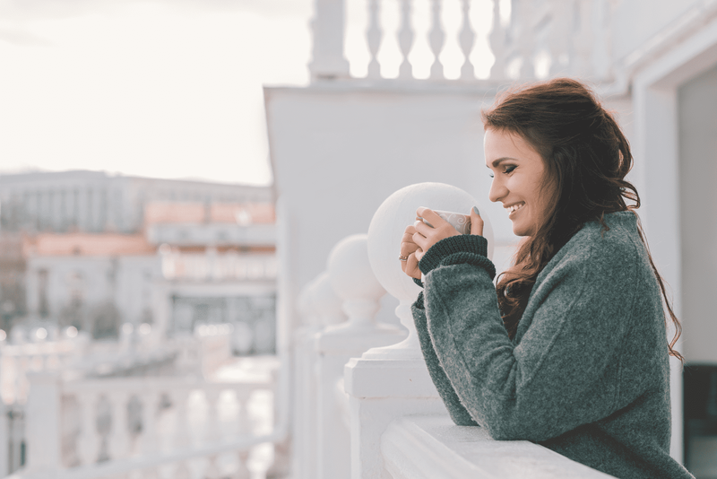 Eine lächelnde Frau steht mit einem Salzstreuer in der Hand auf dem Balkon