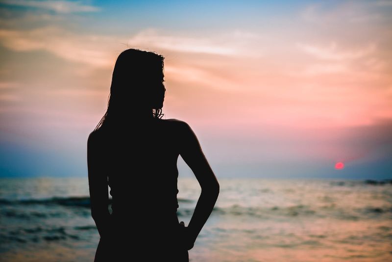 Silhouette einer jungen Frau, die ins Meer starrt