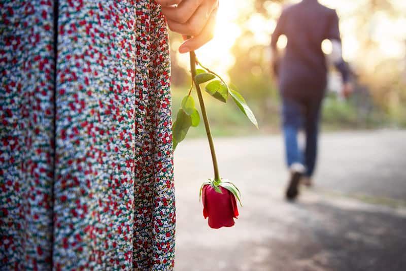 Nahaufnahme einer Frau, die eine Rose hält, während ein Mann weggeht