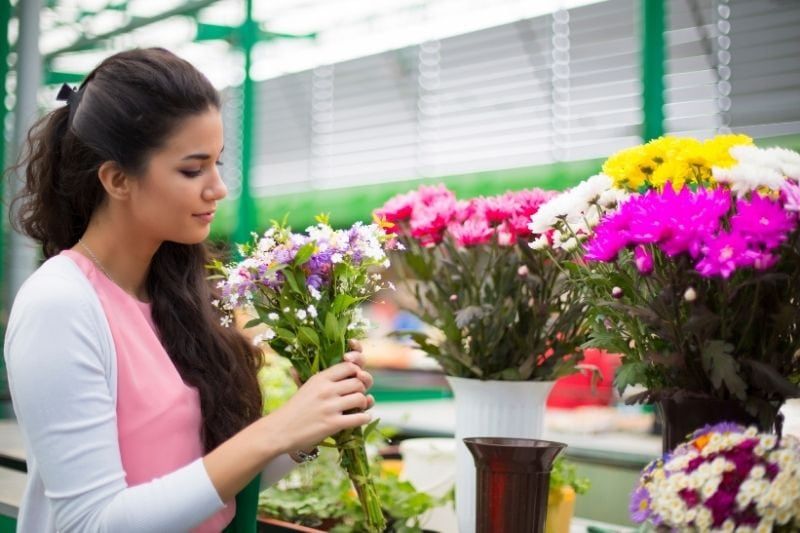 junge Frau, die Blumen auf dem Markt kauft und den Blumenstrauß in der Seitenansicht hält