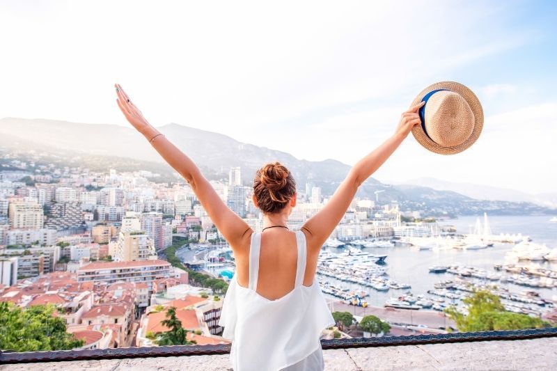 Frau, die allein in Monaco reist und ihre Hände mit ihrem Hut hebt