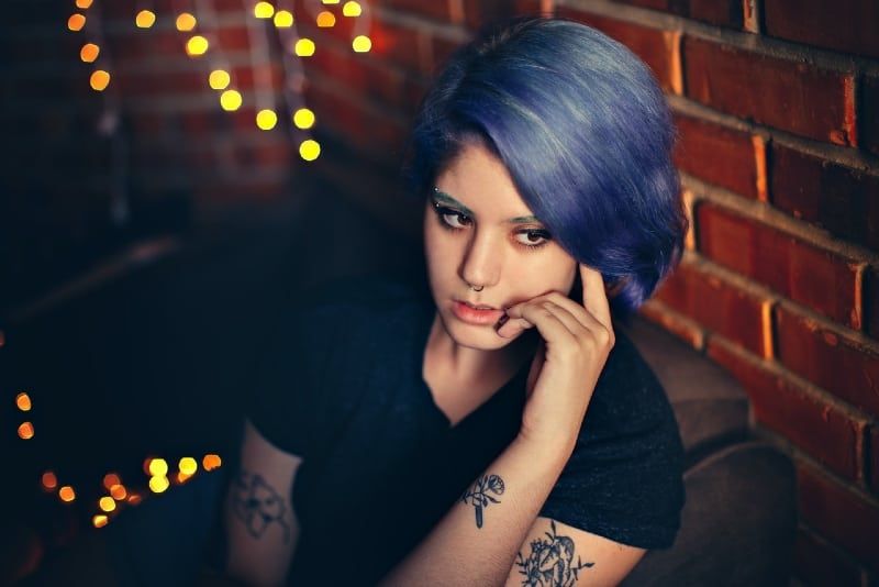 Tätowierte Frau mit blauen Haaren sitzt in der Nähe der Wand