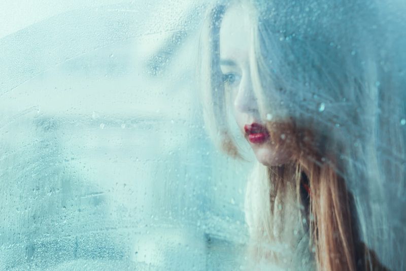 schönes junges Mädchen, das am Fenster steht und den Regen beobachtet