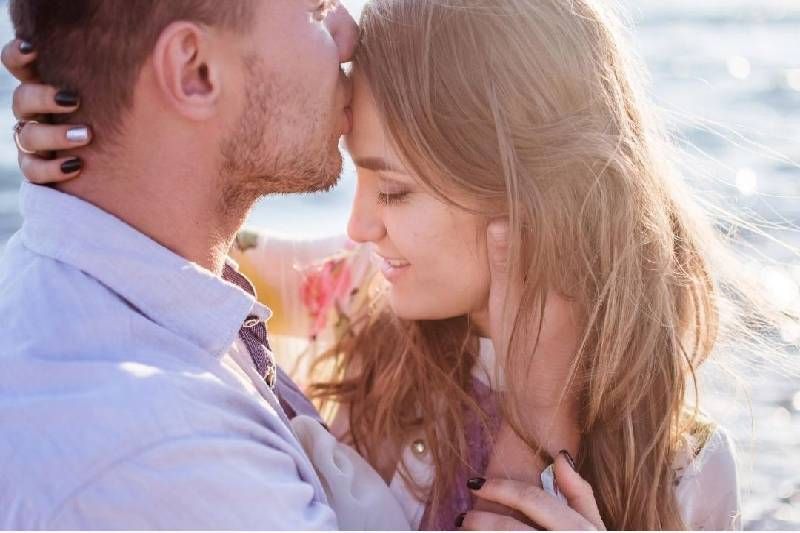 Mann küsst eine Frau im Freien auf die Stirn