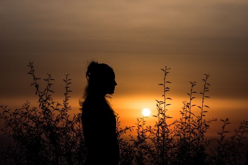 Frau steht bei Sonnenuntergang in der Nähe von Pflanzen