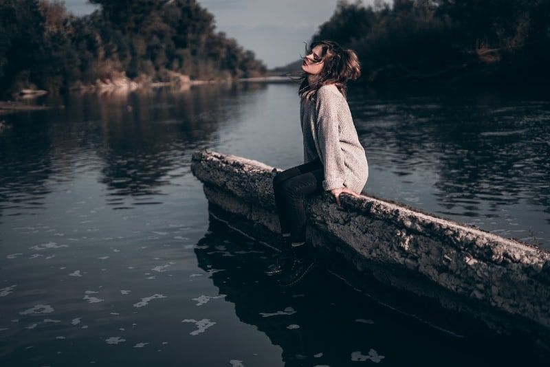 Frau im grauen Pullover sitzt auf Beton in der Nähe von Wasser