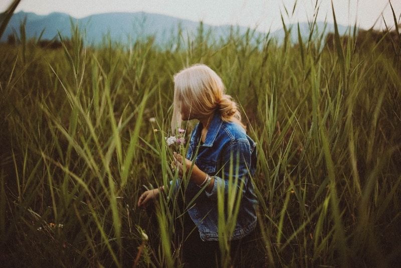 Blonde Frau hält Blumen, während sie auf dem Feld steht