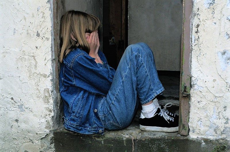 Ein weinendes Kind steht in der Tür und trägt Jeans, die sein Gesicht verdecken