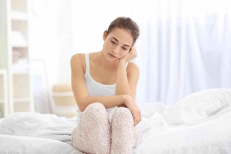 Traurige junge Frau sitzt auf dem Bett
