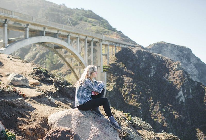 Frau sitzt auf dem Felsen unter der Brücke