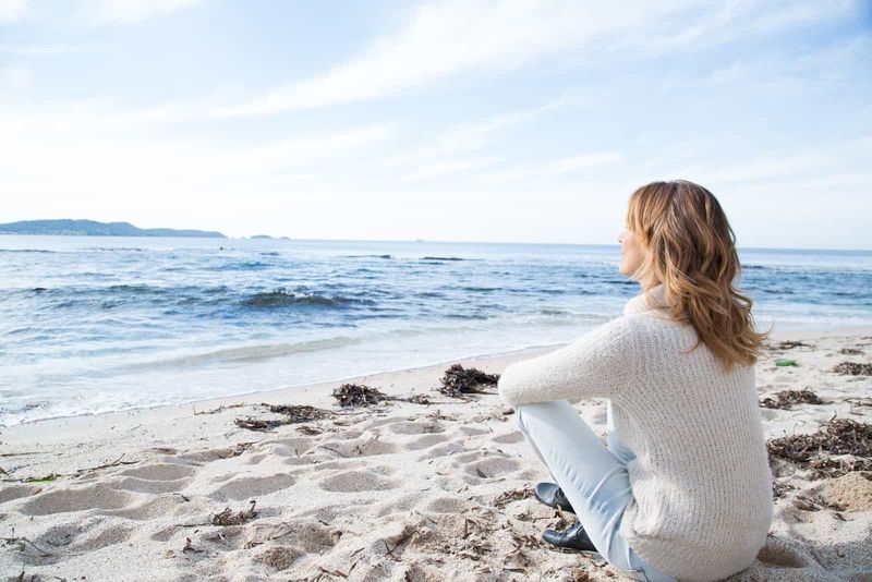 Eine Frau mit langen braunen Haaren sitzt am Strand