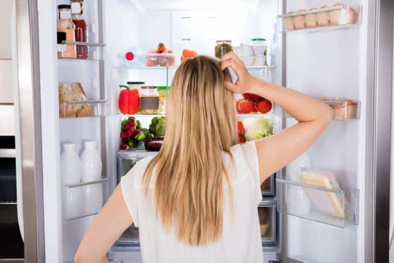 Rückansicht einer verwirrten Frau, die vor einem Kühlschrank steht