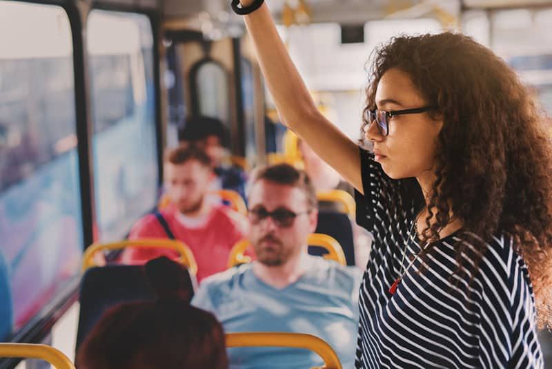 Frau mit lockigem Haar, die eine Brille trägt, während sie in öffentlichen Verkehrsmitteln steht