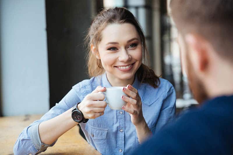 Süße lächelnde Frau hält eine Tasse Kaffee in der Hand und schaut den Mann an